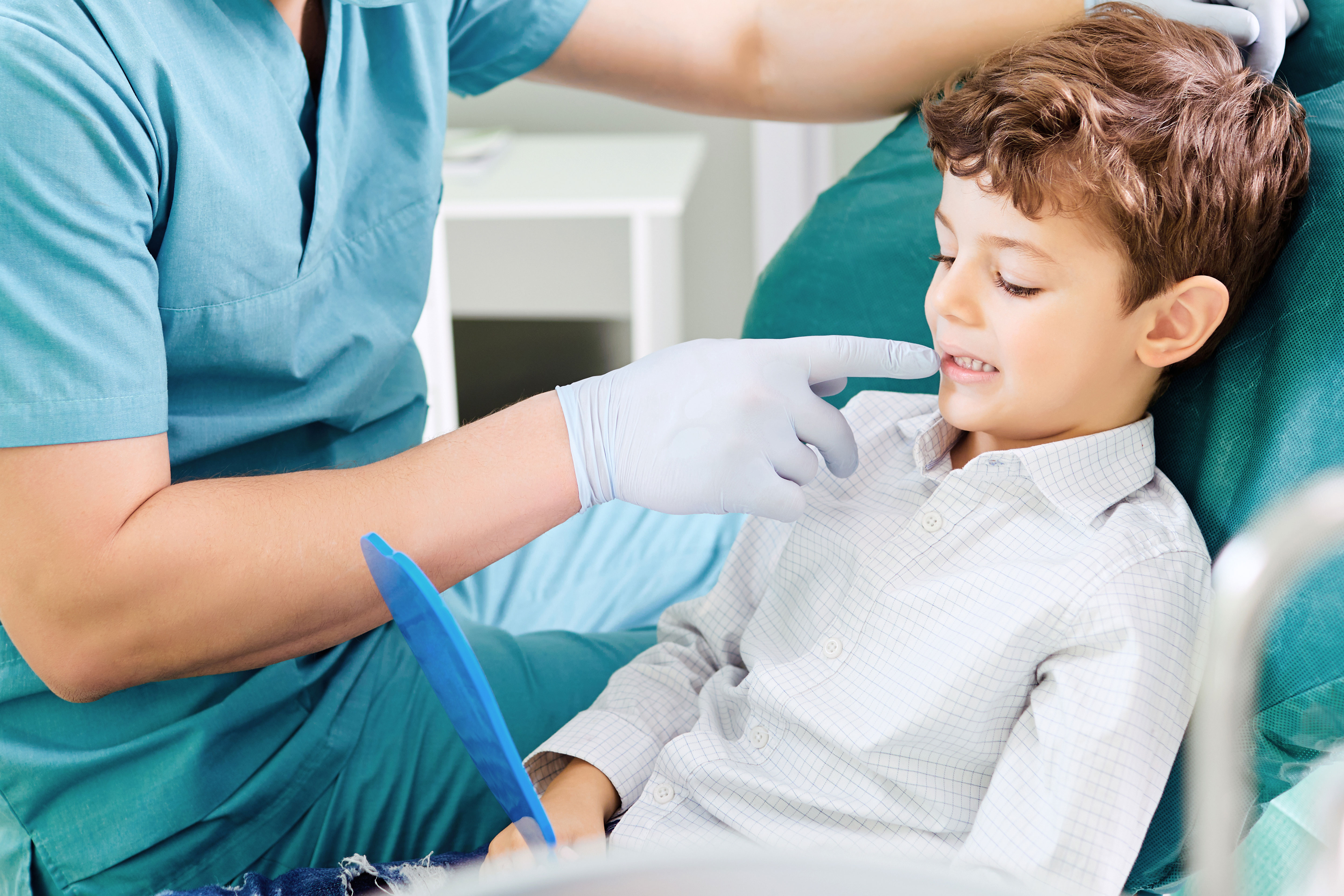 A dental professional examines a young boy's teeth while he sits in a dentist's chair.