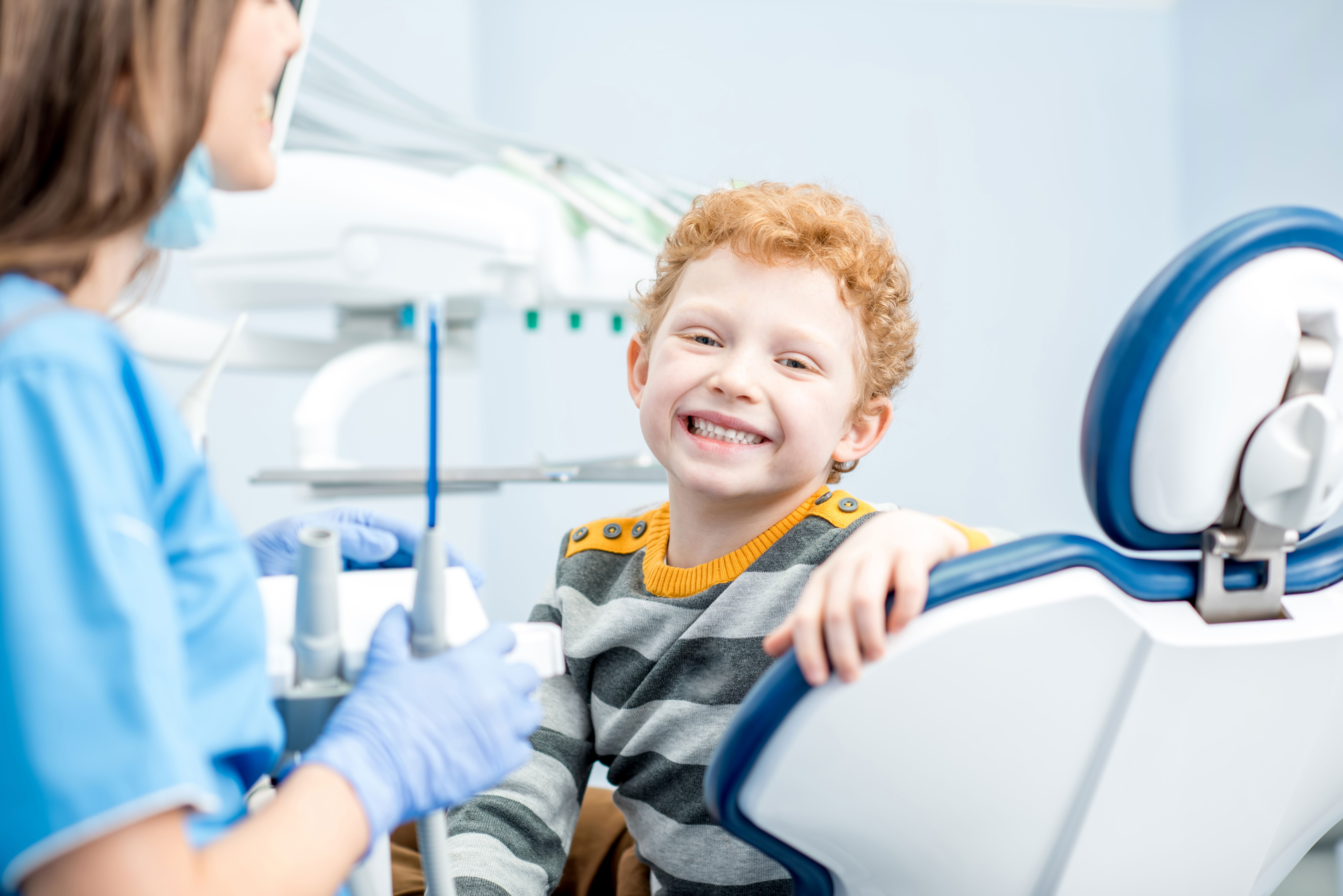 A young boy sitting in a dental chair with a smiling dentist behind him, both wearing face masks.