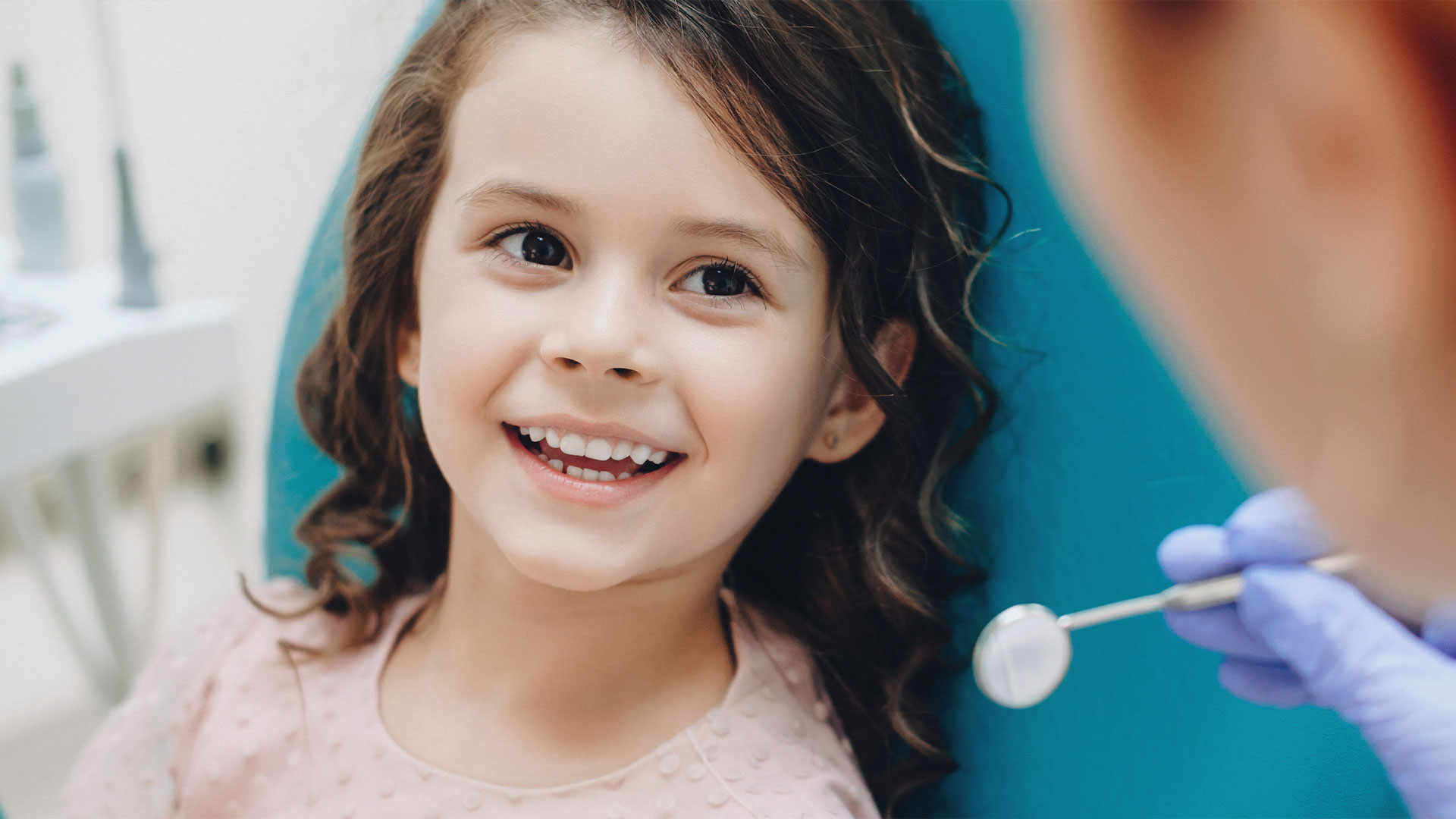 A young girl sitting in a dental chair receiving care from a dentist.
