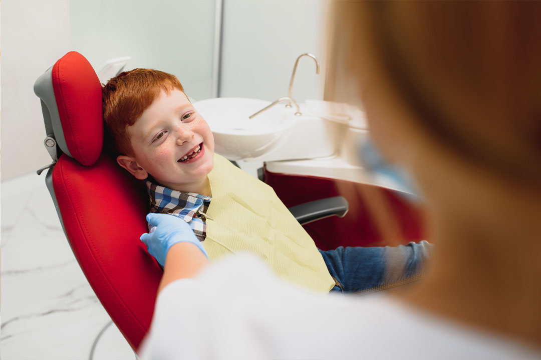 A young boy sitting in a dental chair, receiving dental care from a professional wearing a face mask.