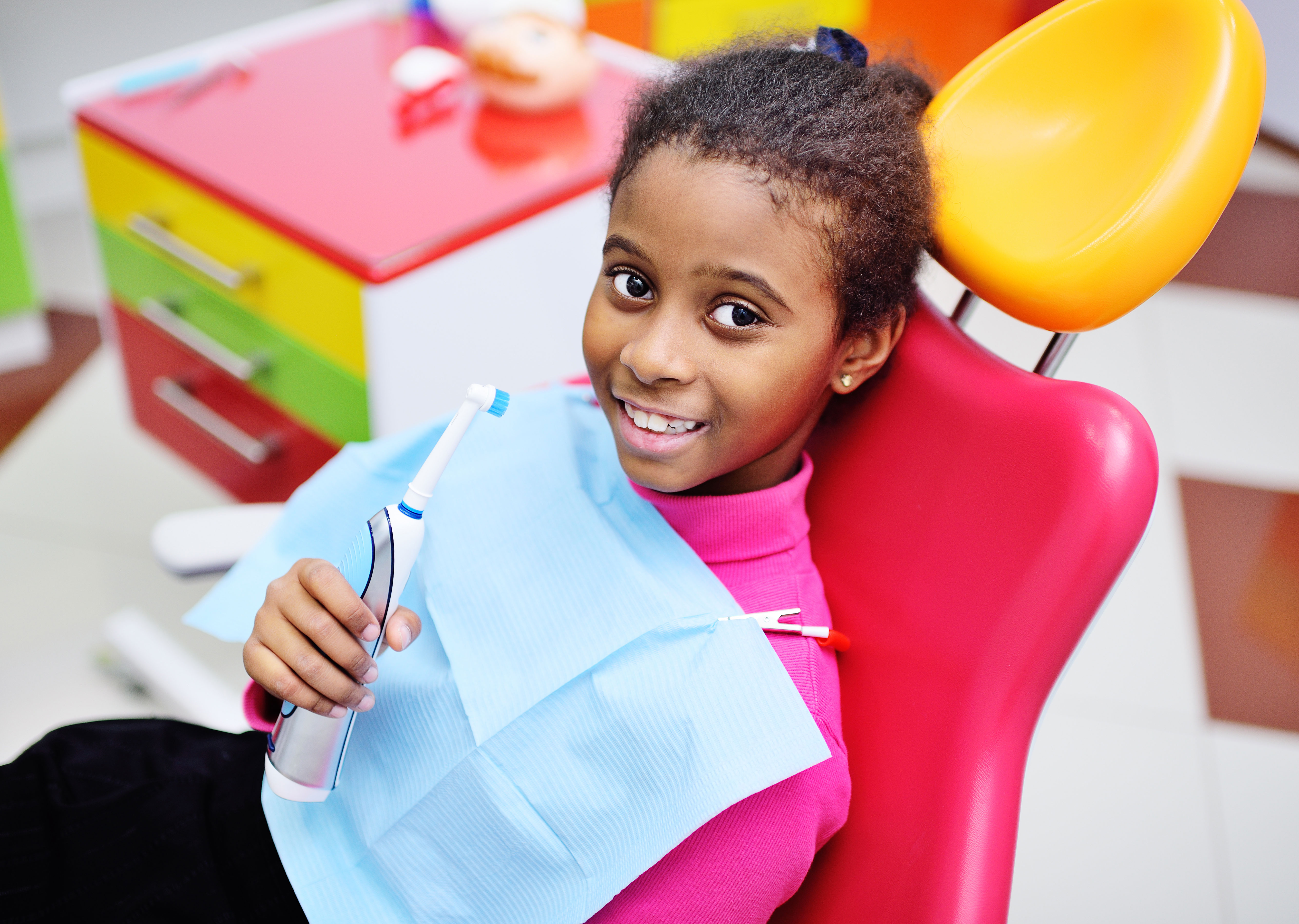 Girl sitting in dental chair holding toothbrush, smiling at camera.